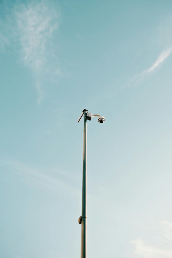 From below of contemporary security camera placing on top of high pillar in city under clear blue sky