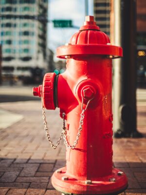 Typical red metal fire hydrant with chain located on paved street on modern city on sunny day