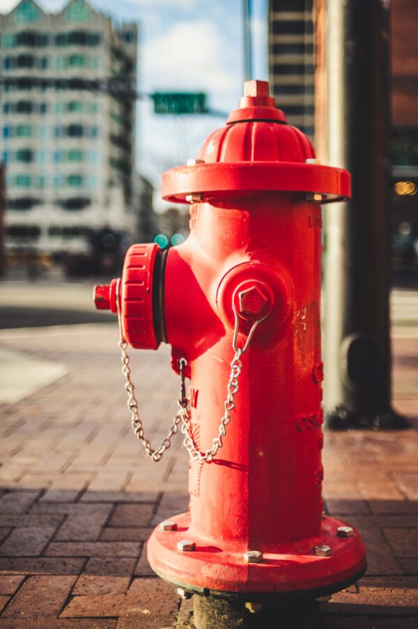 Typical red metal fire hydrant with chain located on paved street on modern city on sunny day